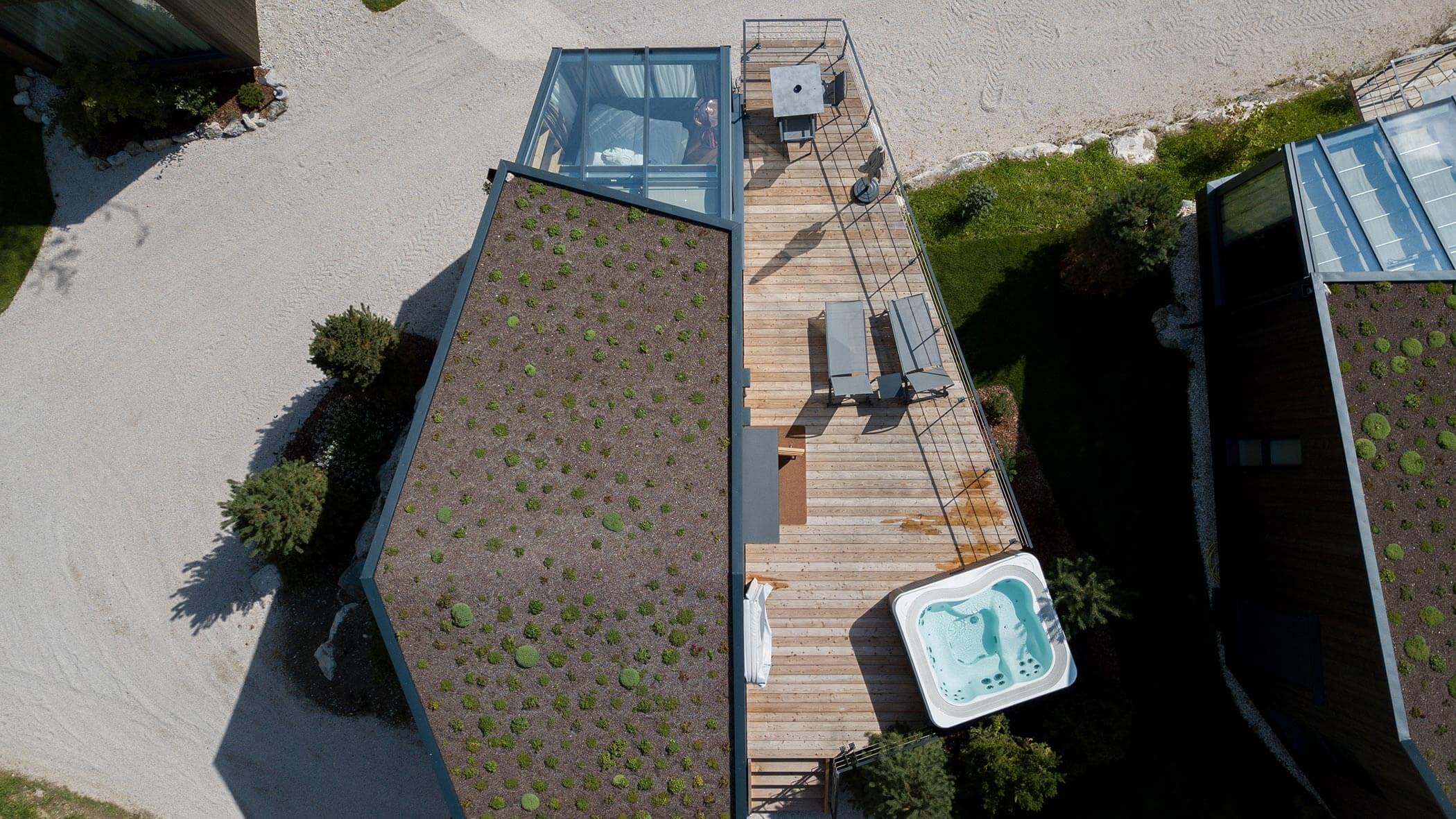 Vista aerea di una terrazza in legno con mobili da esterno e vasca idromassaggio accanto a un edificio con tetto verde. - Skyview Chalets