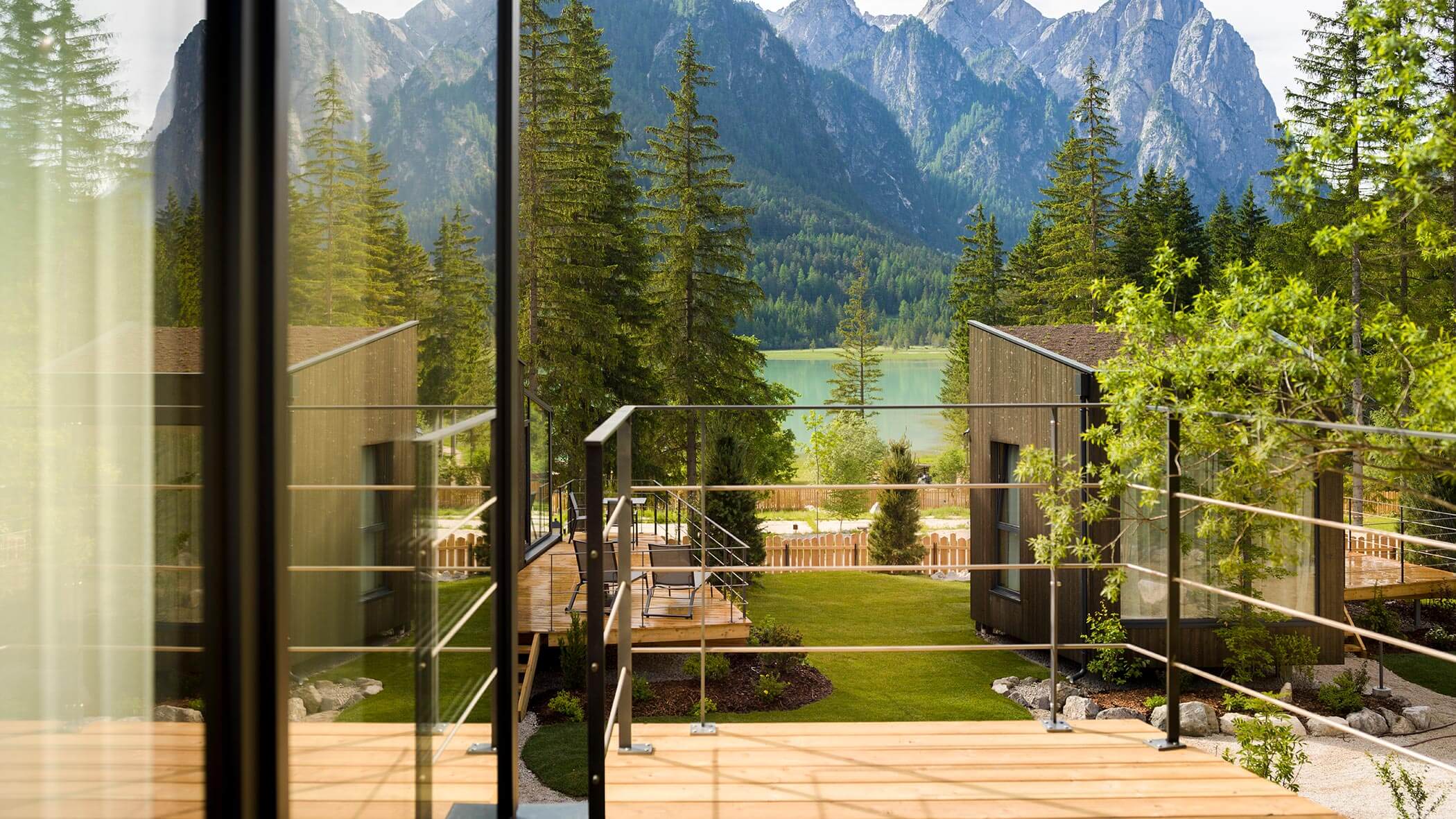 Le moderne cabine e il patio si affacciano su un lago e sulle montagne circondate da alberi nelle giornate di sole. - Skyview Chalets