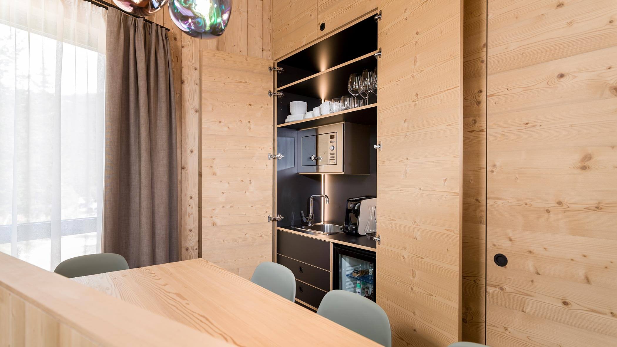 Un piccolo angolo cottura con armadietti in legno aperti, una macchina per il caffè e scaffali per bicchieri e piatti. - Skyview Chalets