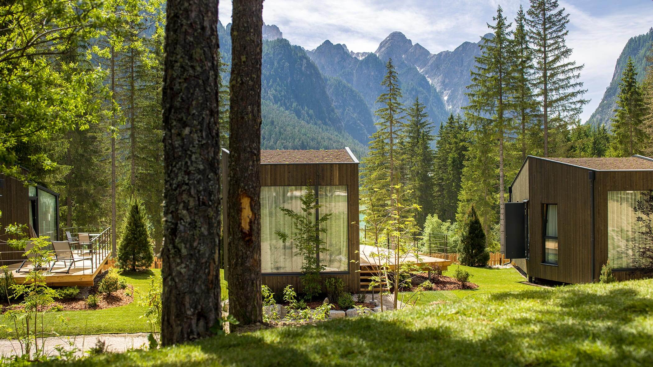 Moderne cabine in legno circondate da alberi, con le montagne sullo sfondo in una giornata di sole. - Skyview Chalets